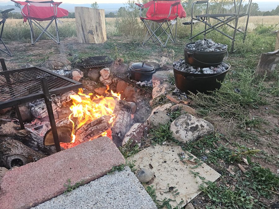 Dutch oven dinner by open fire with red camp chairs